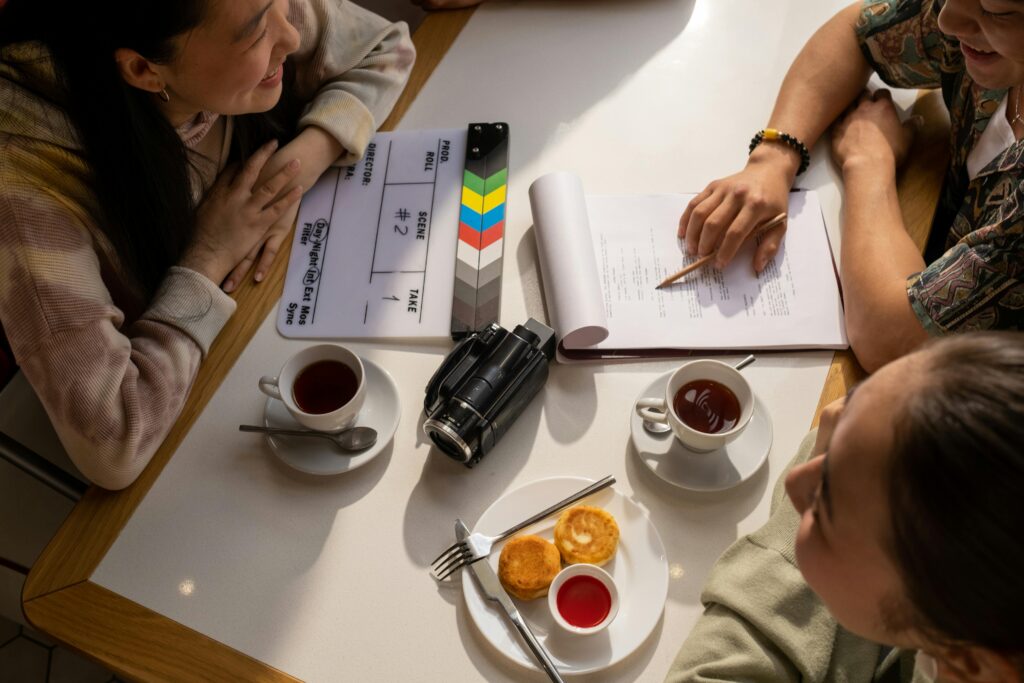 Team discussion over script with a clapperboard, camera, and coffee on a table.